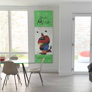 Image of a Denver Art Museum Street Banner hanging in a dining area. Banner features artwork by Joan Miro  entitled Woman, Bird, and Star (Homage to Pablo Picasso) and is framed by a green on the top and bottom of banner.